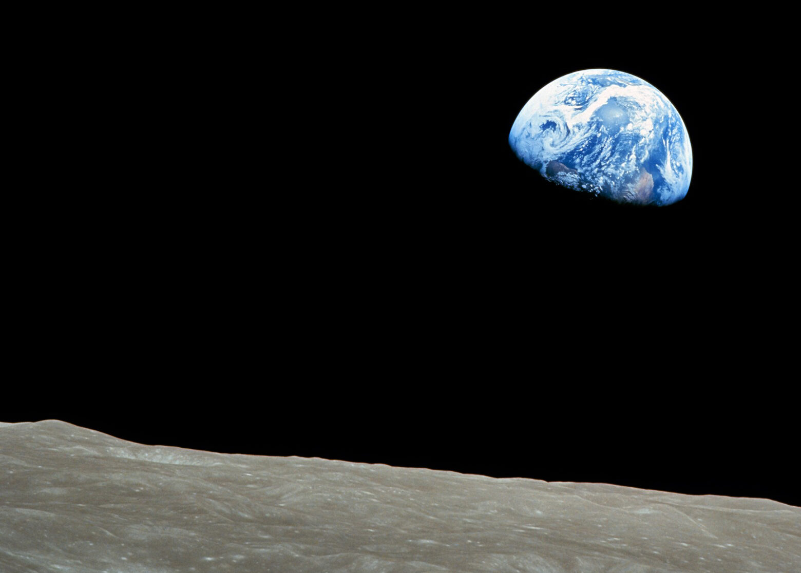 Photo of partial Earth against the blackness of space with the grey landscape of the moon in the foreground.